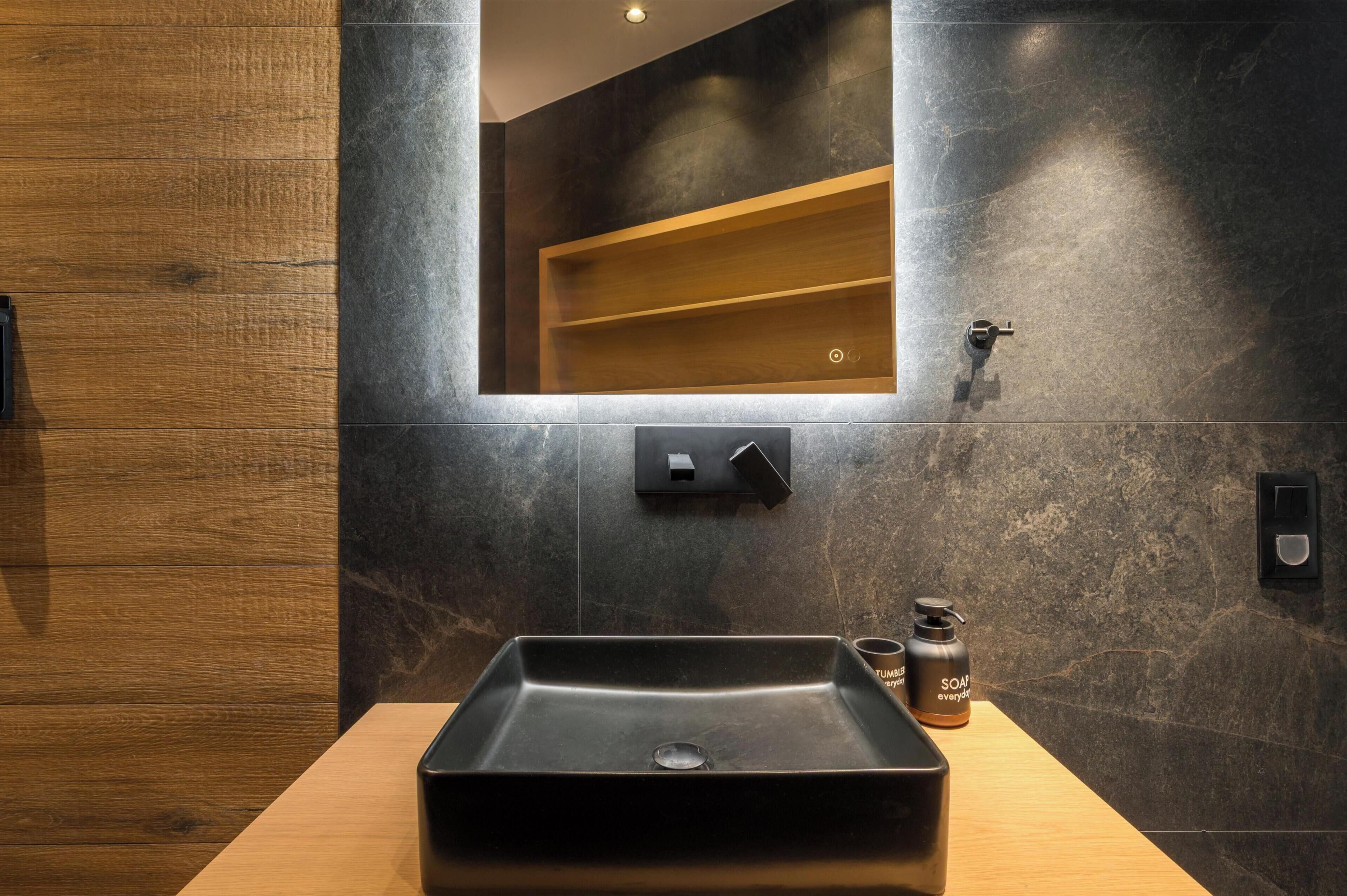 A modern bathroom with a rectangular sink, a wooden vanity, a mirror, and a shelf above the mirror.