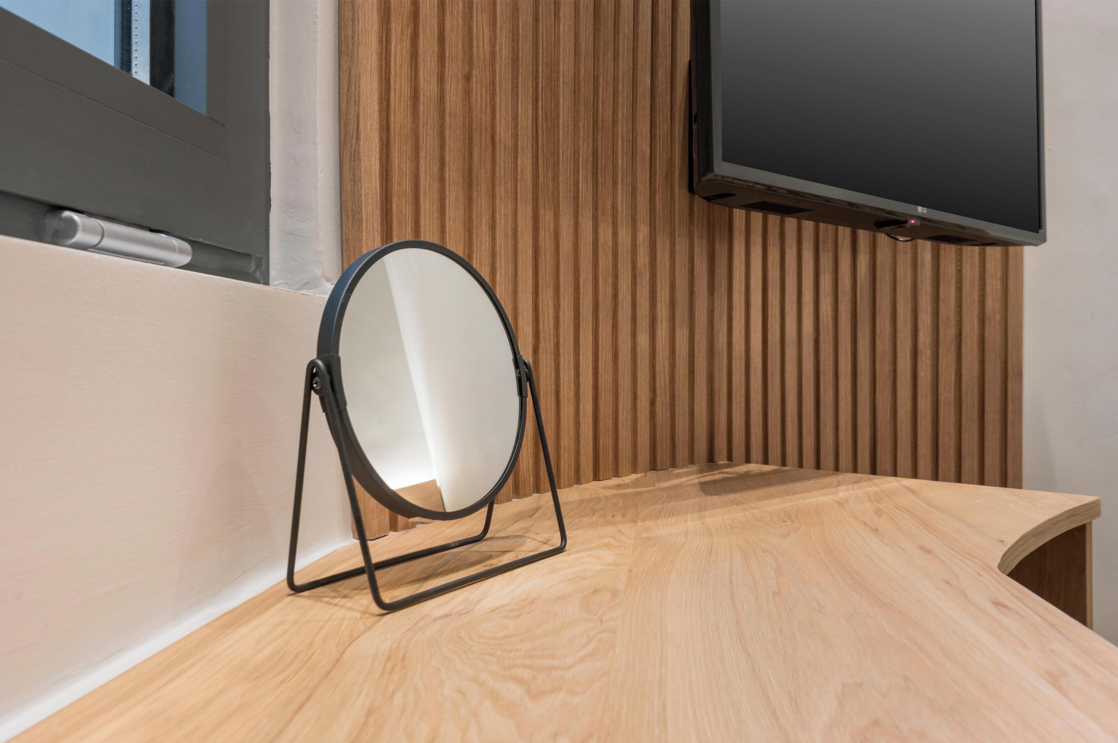 A wooden vanity with a mirror, a flat-screen TV, and a window with blinds.