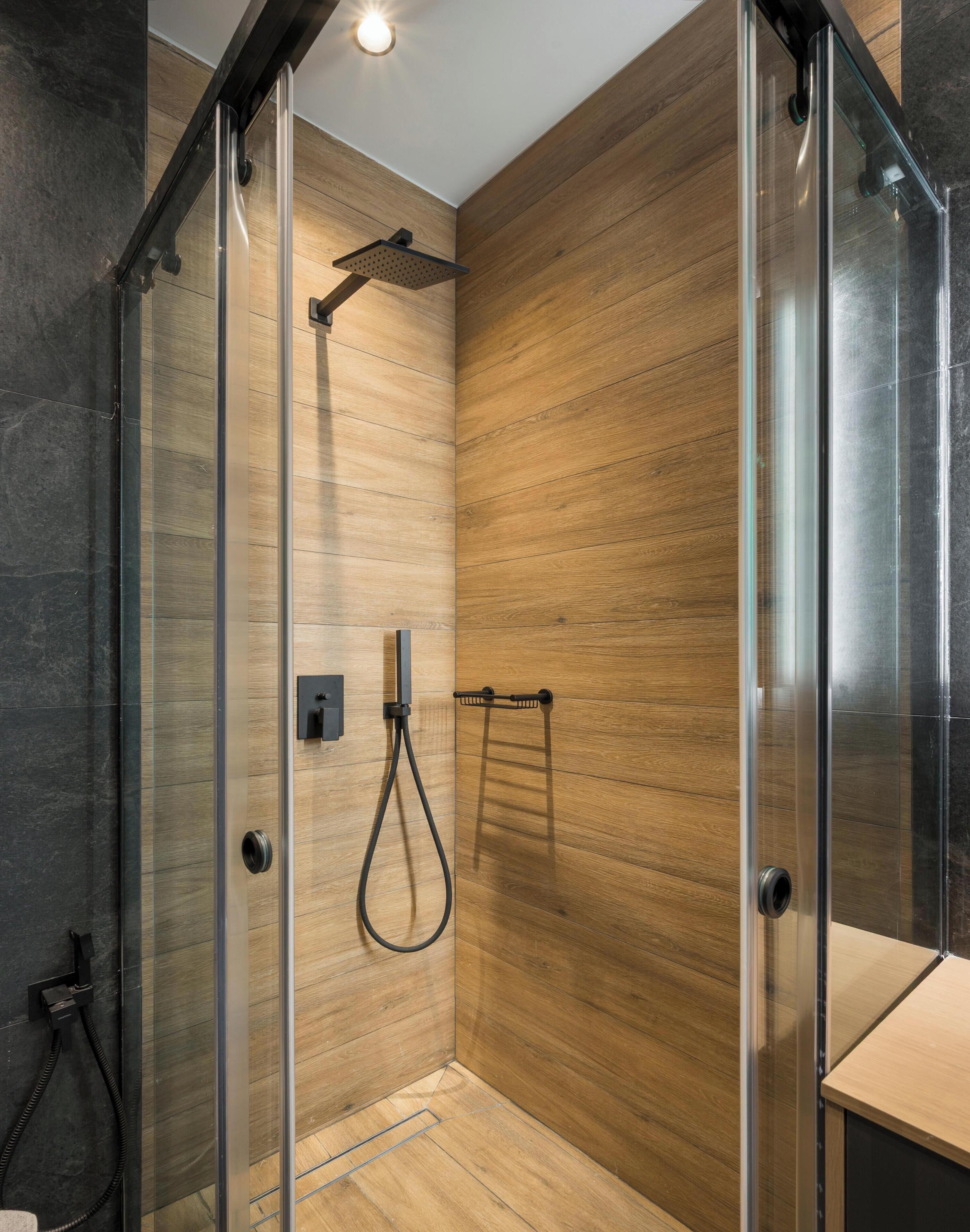 A modern shower enclosure with glass doors, a handheld showerhead, and a towel rack.