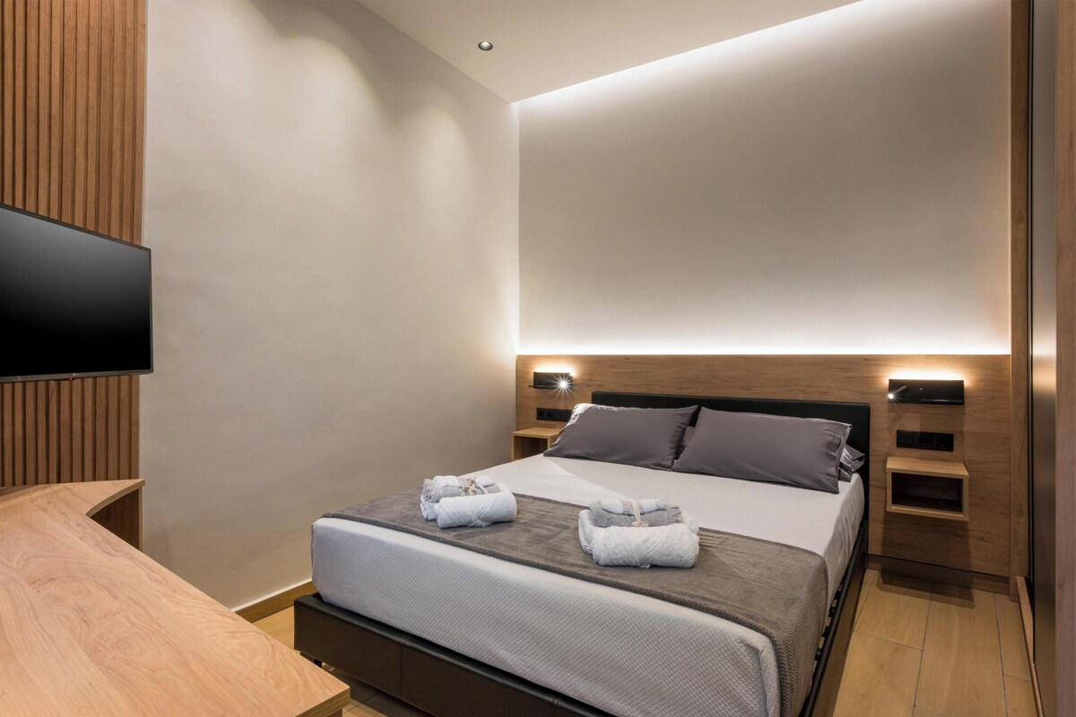 Ein modernes Hotelzimmer mit Bett, Nachttischen, einem Flachbildfernseher und einer Wand mit Holzverkleidung.