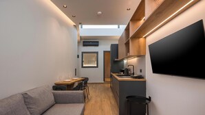 Ein kompakter Wohnbereich mit Sofa, Essplatz, Küchenzeile und Wand-Fernseher.