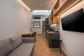 Ein kompakter Wohnbereich mit Sofa, Essplatz, Küchenzeile und Wand-Fernseher.