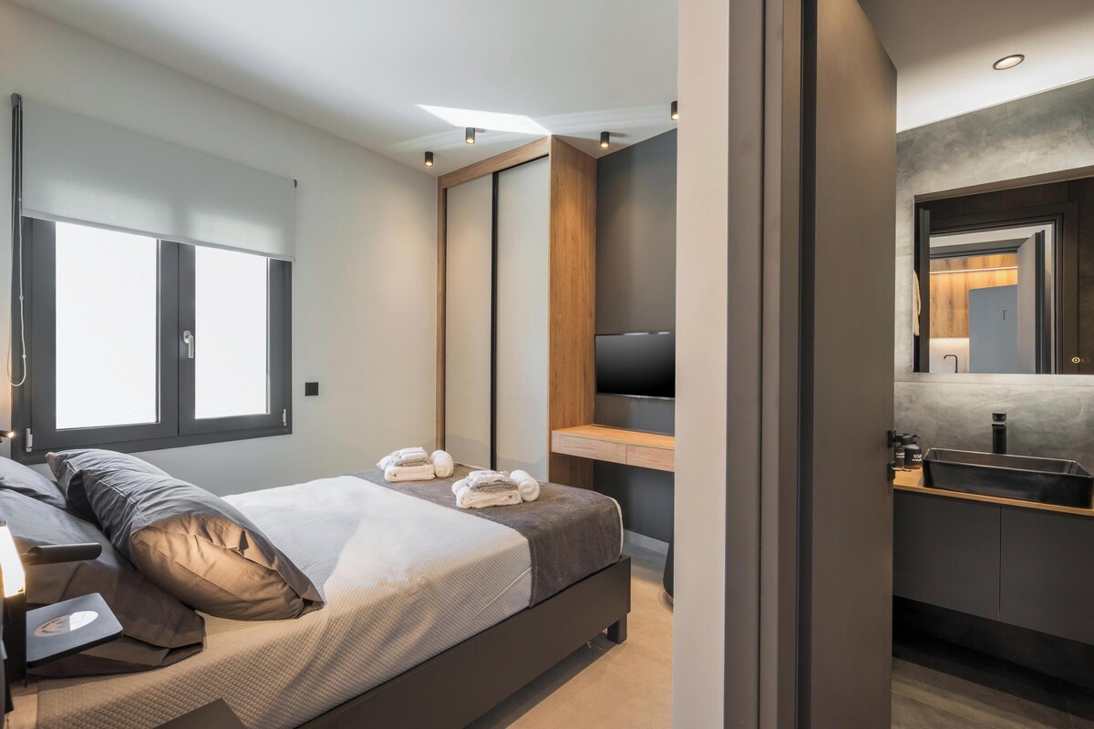 Ein modernes Schlafzimmer mit einem Bett, einem Fernseher, einem Holztisch und einem Badezimmer mit einem Waschbecken.