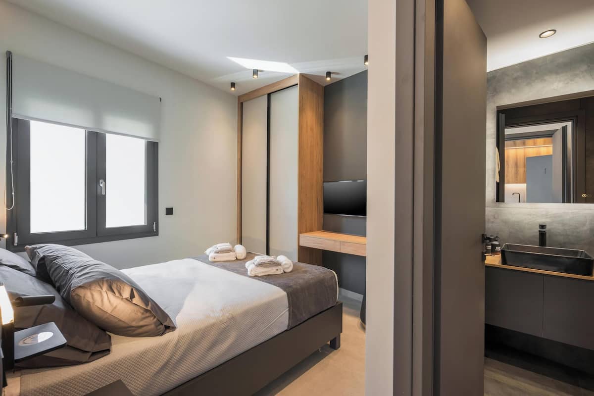 Ein modernes Schlafzimmer mit einem Bett, einem Fernseher, einem Holztisch und einem Badezimmer mit einem Waschbecken.