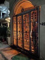 Una entrada protegida por una reja con detalles metálicos decorativos, un balcón visible y una planta en maceta.