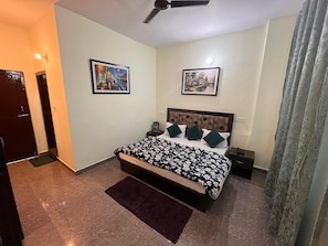 Une chambre à coucher comprenant un lit, deux tables de chevet, un ventilateur de plafond et deux tableaux encadrés accrochés au mur.