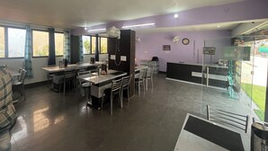 En restaurang med en receptionsdisk, flera bord och stolar samt stora fönster med gardiner.