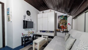 Ein Zimmer mit einem Bett, einem Fernseher, einem weißen Kleiderschrank, einem kleinen Tisch und einer Wanddekoration.