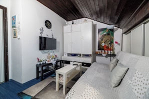 Ein Zimmer mit einem Bett, einem Fernseher, einem weißen Kleiderschrank, einem kleinen Tisch und einer Wanddekoration.
