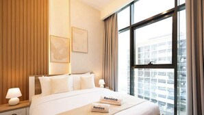 Habitación de hotel con una cama grande, una mesita de noche, una lámpara, una ventana con cortinas y dos cuadros en la pared.