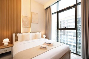 A hotel room with a large bed, a nightstand, a lamp, a window with curtains, and two framed pictures on the wall. - Rentico l Luxury 1BR Pool View l Azizi Riviera (Dubai)