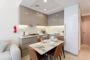 A modern kitchen with a dining table set for four, a built-in oven, and a refrigerator. - Rentico l Luxury 1BR Pool View l Azizi Riviera (Dubai)