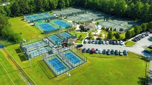 Vue aérienne d’un complexe de tennis comprenant plusieurs courts, un parking et des espaces verts environnants.