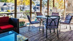 Un espace extérieur abrité, doté d’une table et de chaises, d’un canapé rouge et offrant une vue sur les maisons à travers de grandes fenêtres.