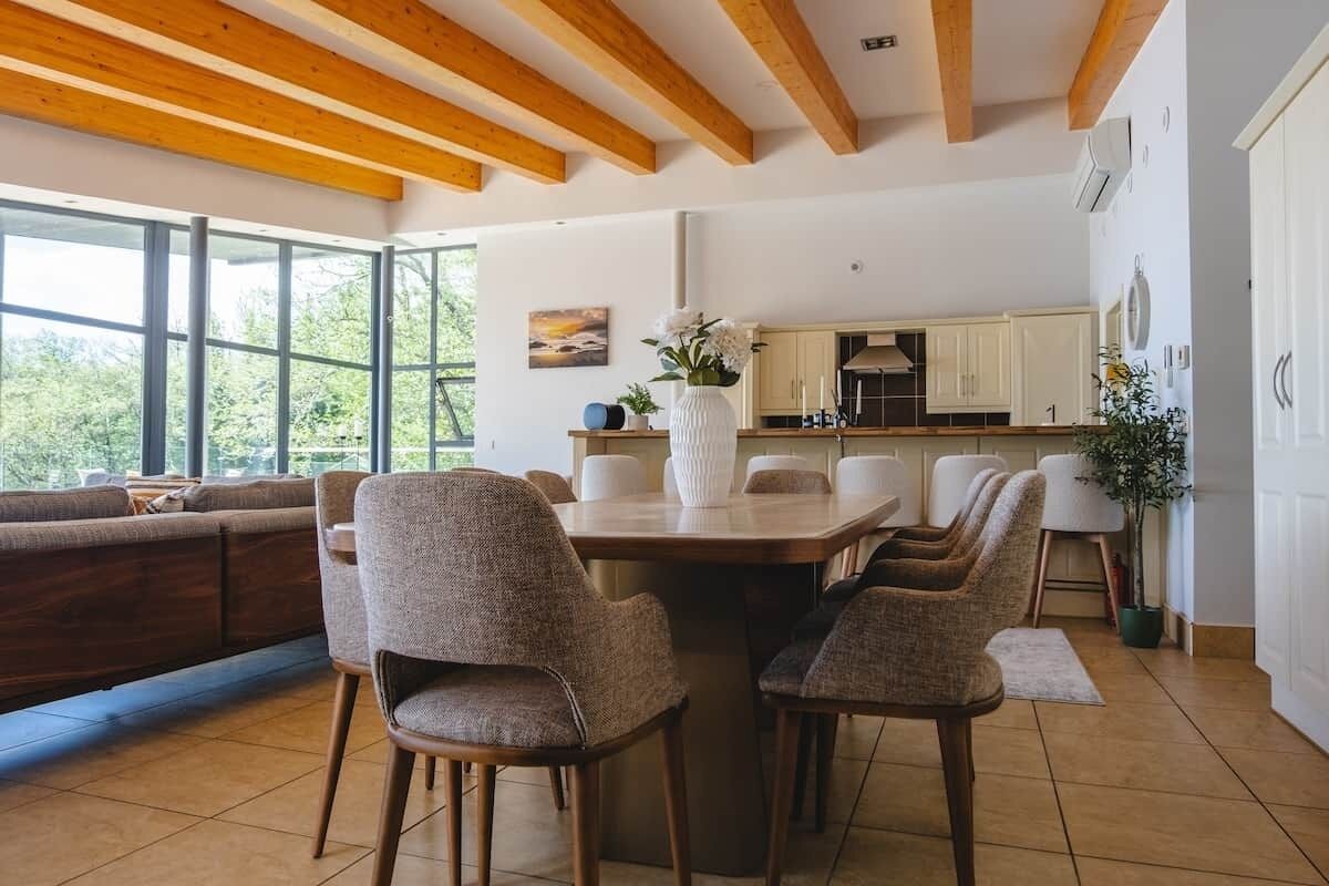 Una cocina moderna con armarios blancos, un comedor con mesa y sillas de madera, y amplios ventanales con vistas al verdor.