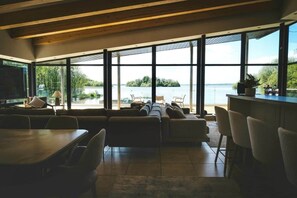 Un intérieur moderne avec une grande fenêtre donnant sur un plan d’eau et un espace verdoyant.
