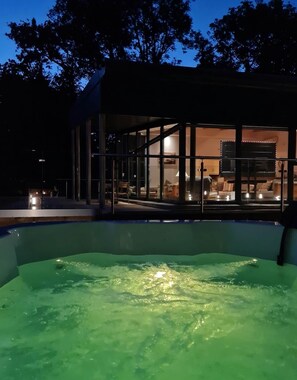 Un espace piscine doté d’une structure en verre, d’un jacuzzi et d’un coin salon avec un téléviseur.