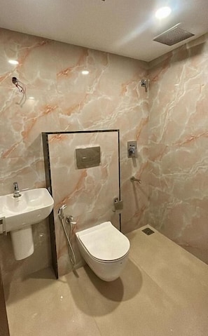Een badkamer met een marmeren wand, een wastafel, een toilet en een douche.
