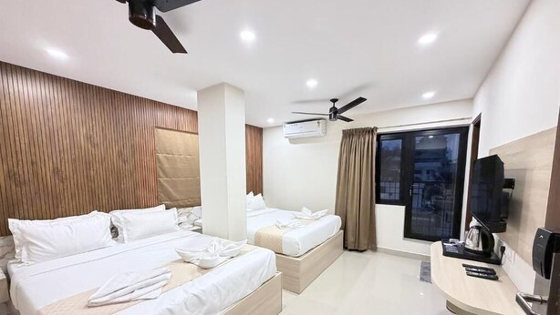 Habitación de hotel con dos camas, televisión, escritorio y ventilador de techo.