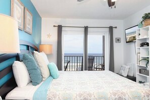 Ein Schlafzimmer mit Bett, Nachttisch, Fernseher, Bücherregal und einem Balkon mit Meerblick.