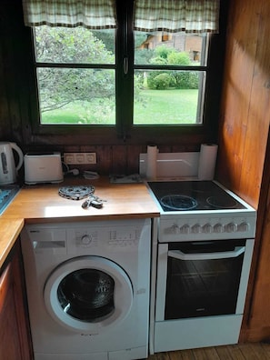 Una cocina compacta con lavadora, horno, cocina y ventana con vistas a zonas verdes.
