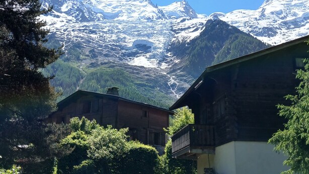 Un pueblo de montaña con casas de madera, un patio cubierto de hierba y montañas nevadas al fondo.