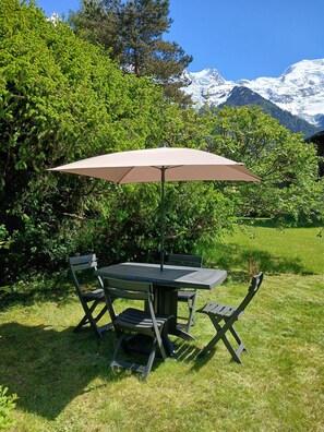 Una mesa redonda con una sola silla, un paraguas y vistas de montañas nevadas.