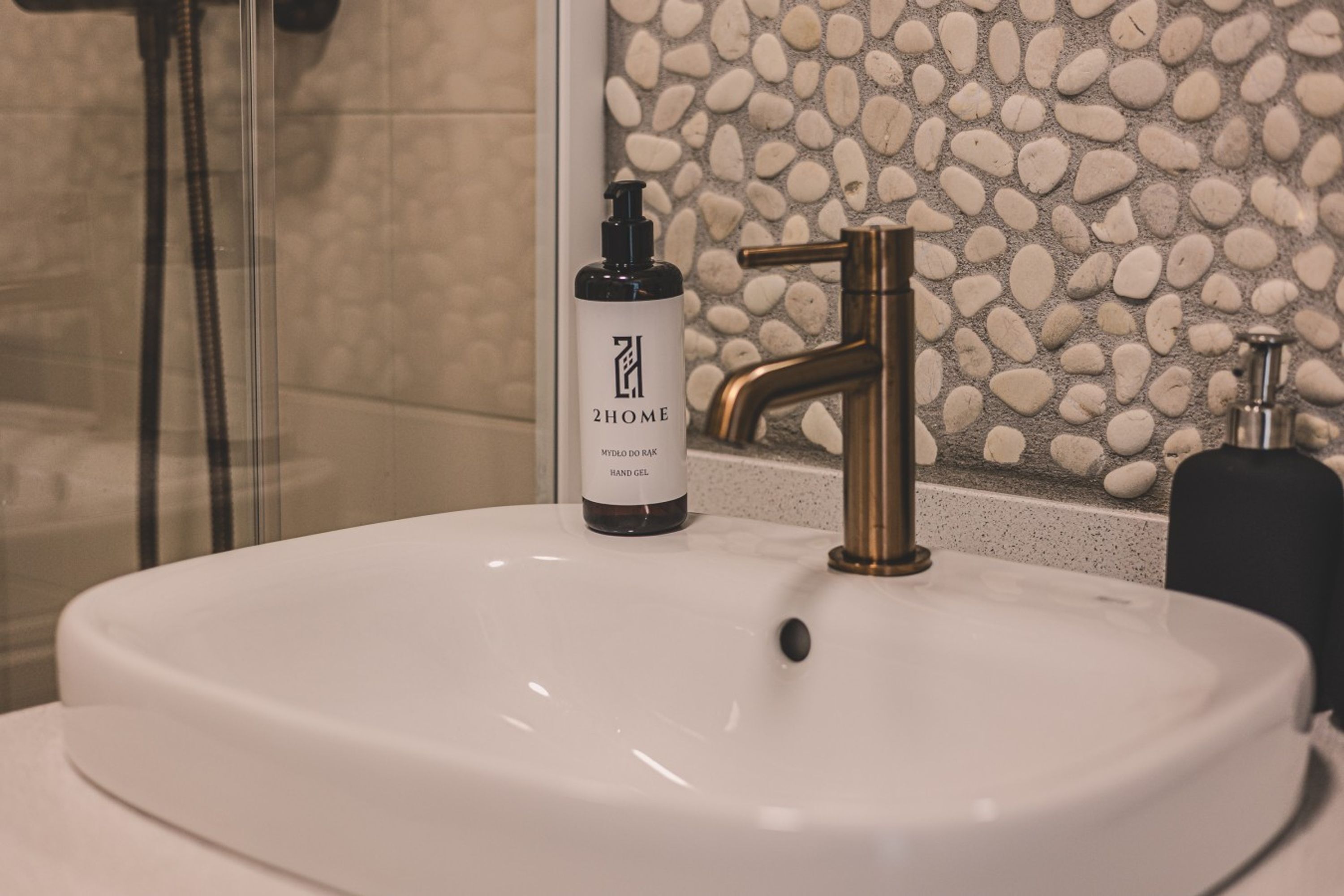A bathroom with a white sink, a gold faucet, and a bottle of hand gel labeled '2HOME MYYLO DO RA HAND GEL'.