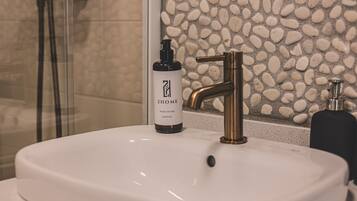 A bathroom with a white sink, a gold faucet, and a bottle of hand gel labeled '2HOME MYYLO DO RA HAND GEL'.