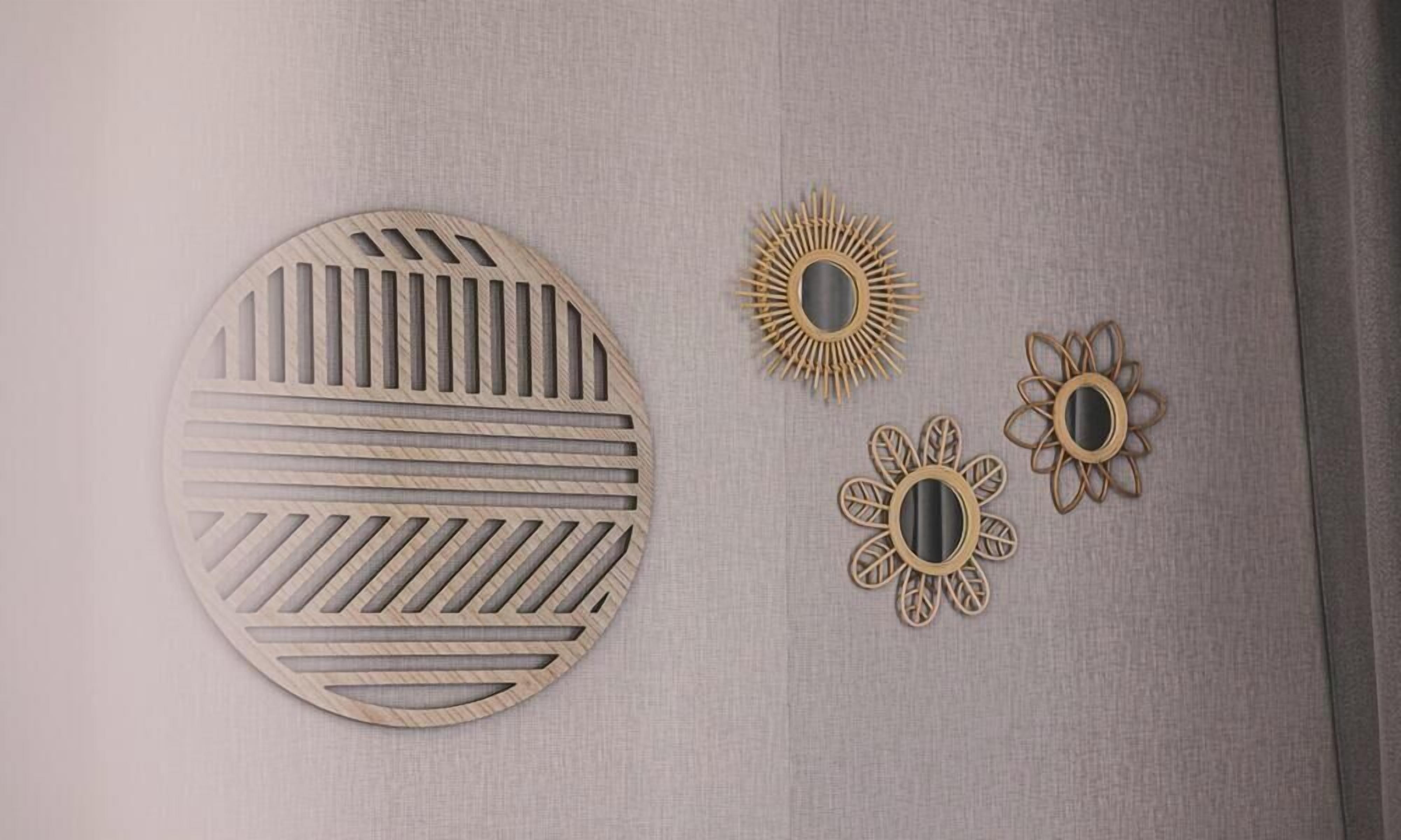 A wall with three decorative wall art pieces: a large circular piece with horizontal lines, a smaller circular piece with a sun-like design, and a smaller piece with a floral pattern.