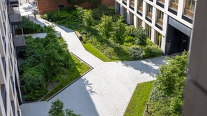 A modern building with a courtyard featuring a geometric pathway, surrounded by greenery and adjacent to a brick building. - Musa Nowoczesne wn Trze w Sercu Miasta Nowy Port (gmina Parzęczew)