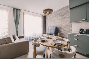 A modern living room with a sofa, dining table set for four, and a kitchen area with cabinets and a coffee machine.