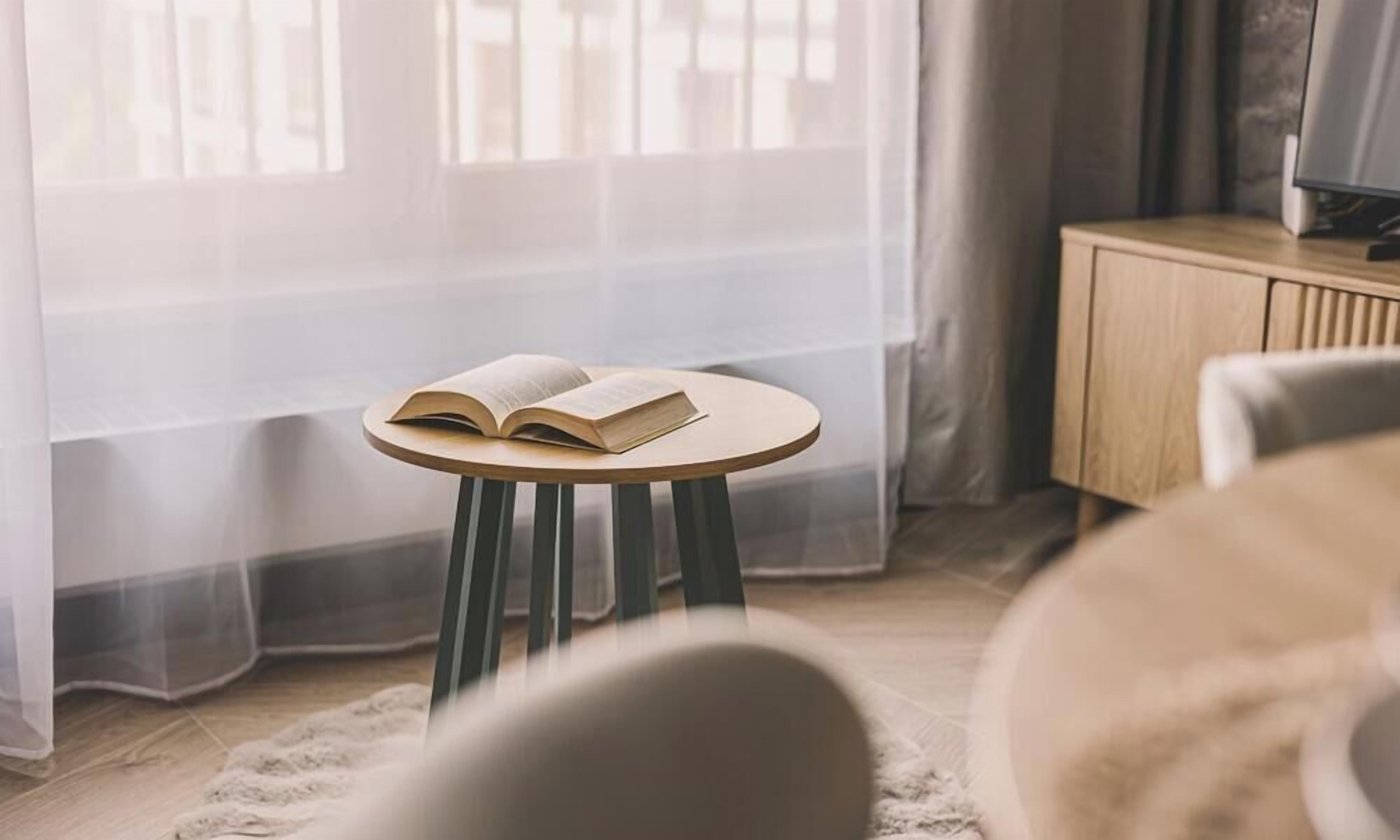 A room with a round wooden table, a book, a chair, and a cabinet.