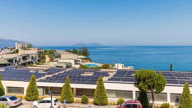 A coastal residential area with solar panels, parked cars, and a clear view of the sea. - Ocean Horizon Apartment Sea View Parking (Vlorë)
