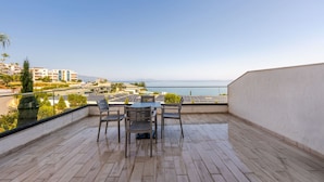 A wooden deck with a table and chairs, overlooking a coastal area with buildings and a clear sky. - Ocean Horizon Apartment Sea View Parking (Vlorë)