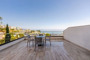 Eine Holzterrasse mit Tisch und Stühlen, mit Blick auf eine Küstenlandschaft mit Gebäuden und einem klaren Himmel.