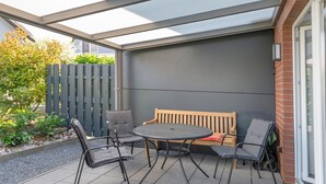 Un portico coperto con un tavolo rotondo e quattro sedie, una panca di legno e un muro in mattoni.