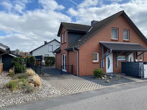 Une maison à deux étages avec une façade en briques, un toit en tuiles et un petit porche à l’avant.