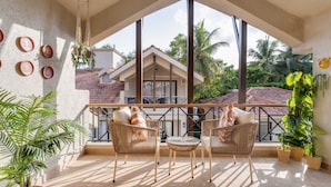 A balcony with wicker furniture, potted plants, and a view of a house with a tiled roof. - Casa Calma Scenic 3BR Duplex With Jacuzzi (Oxel)
