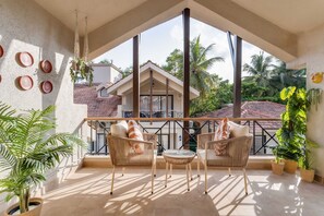 A balcony with wicker furniture, potted plants, and a view of a house with a tiled roof. - Casa Calma Scenic 3BR Duplex With Jacuzzi (Oxel)