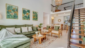 A living room with a green sofa, wooden coffee table, and a staircase with a chandelier. - Casa Calma Scenic 3BR Duplex With Jacuzzi (Oxel)