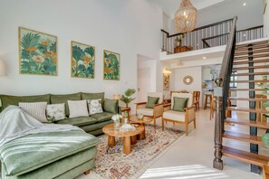 A living room with a green sofa, wooden coffee table, and a staircase with a chandelier. - Casa Calma Scenic 3BR Duplex With Jacuzzi (Oxel)