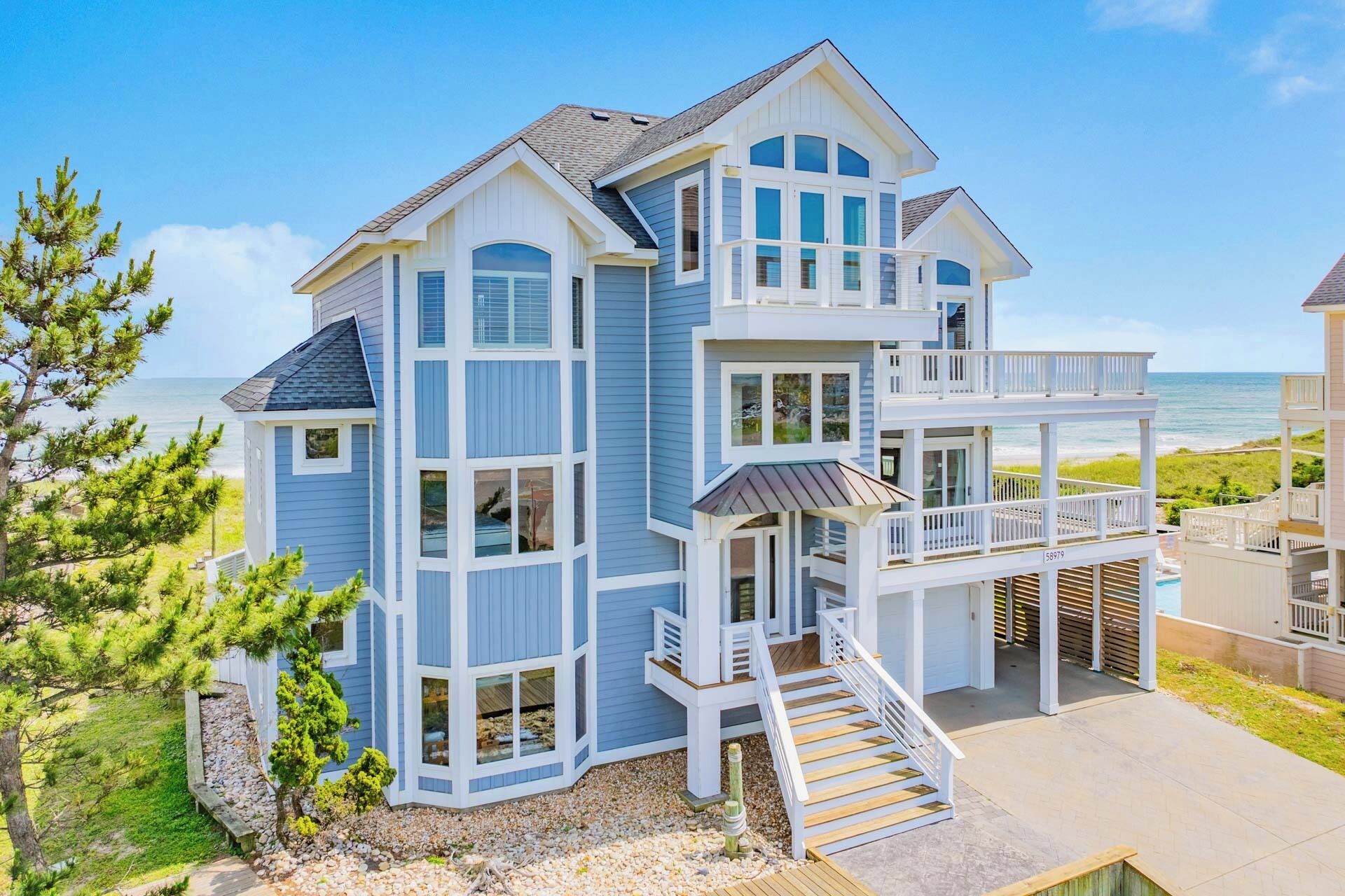 Ein mehrstöckiges Strandhaus mit Balkon und einer Treppe, die zum oberen Stockwerk führt, mit Blick auf den Ozean.