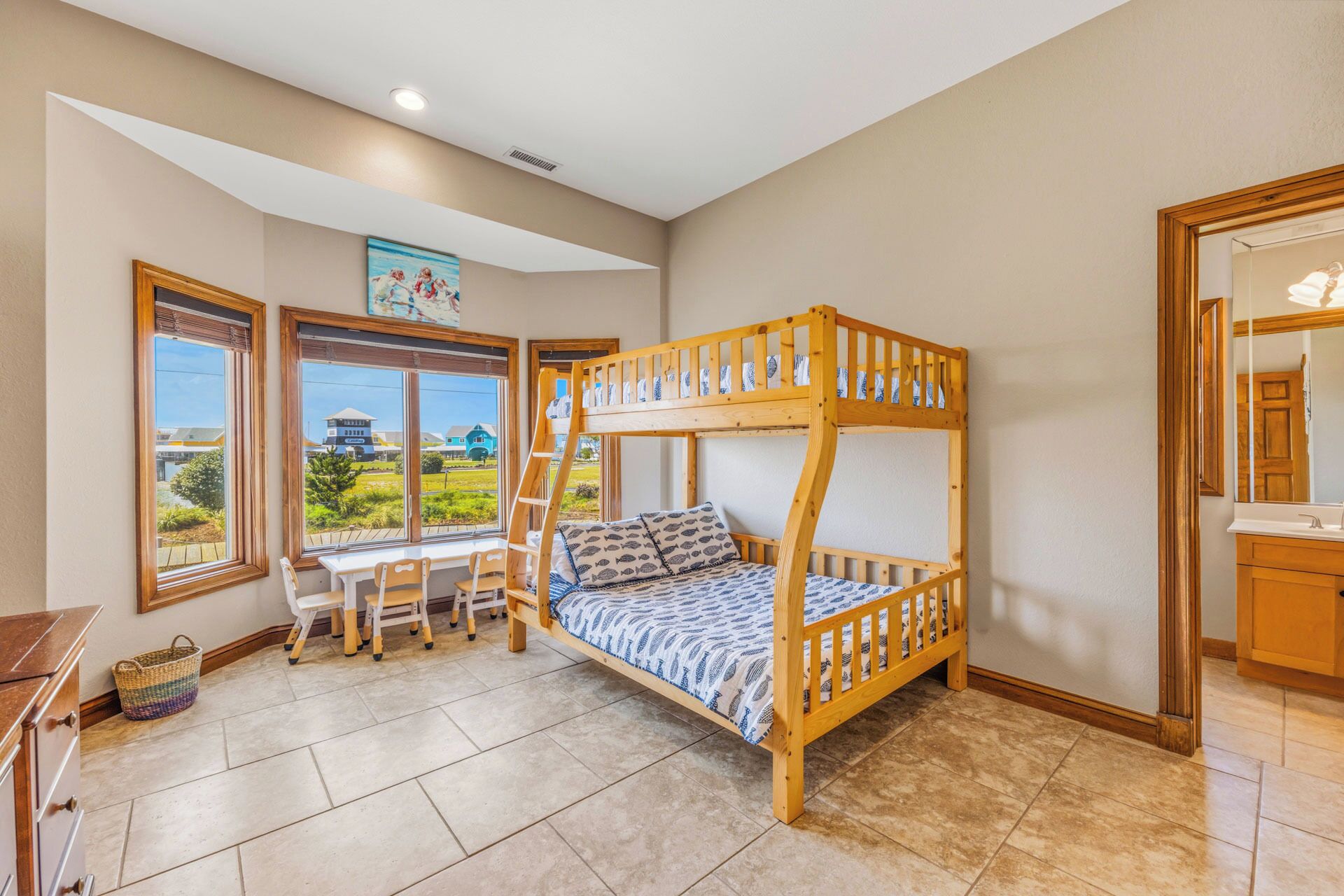 Una cama litera con vista a casas, un escritorio con sillas y una ventana con persianas.