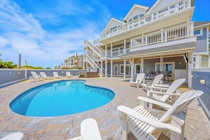 A pool area with lounge chairs and a two-story building with balconies. - Oceanfront, Dog Friendly Home in Hatteras with Pool, Hot Tub, Game Room (Hatteras)