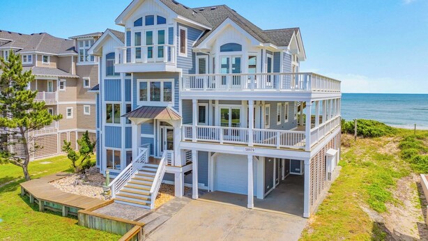 A multi-story beachfront house with a balcony, a covered porch, and a garage.