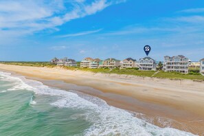 A beachfront property with multiple houses, a sandy beach, and ocean waves. - Oceanfront, Dog Friendly Home in Hatteras with Pool, Hot Tub, Game Room (Hatteras)
