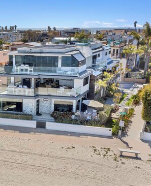 Una casa moderna de varios pisos con fachada de vidrio, mobiliario exterior y vista al mar.