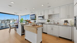 Une cuisine moderne avec des meubles blancs, un îlot central et une vue sur l’extérieur.