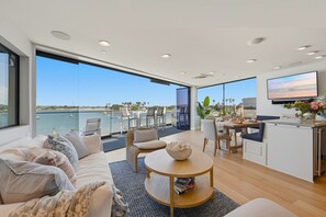 Un espacio habitable moderno con un amplio ventanal con vista a un puerto deportivo, una zona de comedor y una cocina.